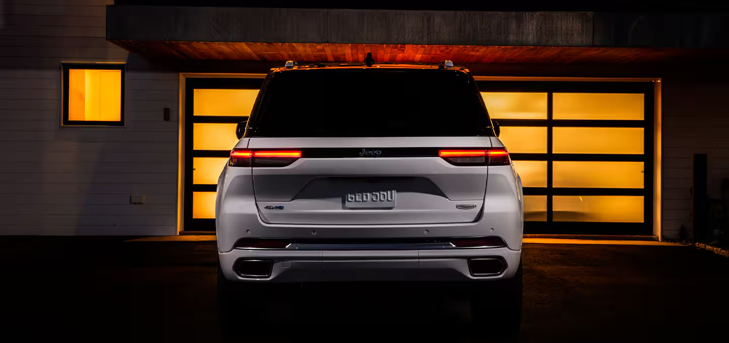 The rear of a 2025 Jeep Grand Cherokee Summit Reserve 4xe, parked in front of a lighted garage door.