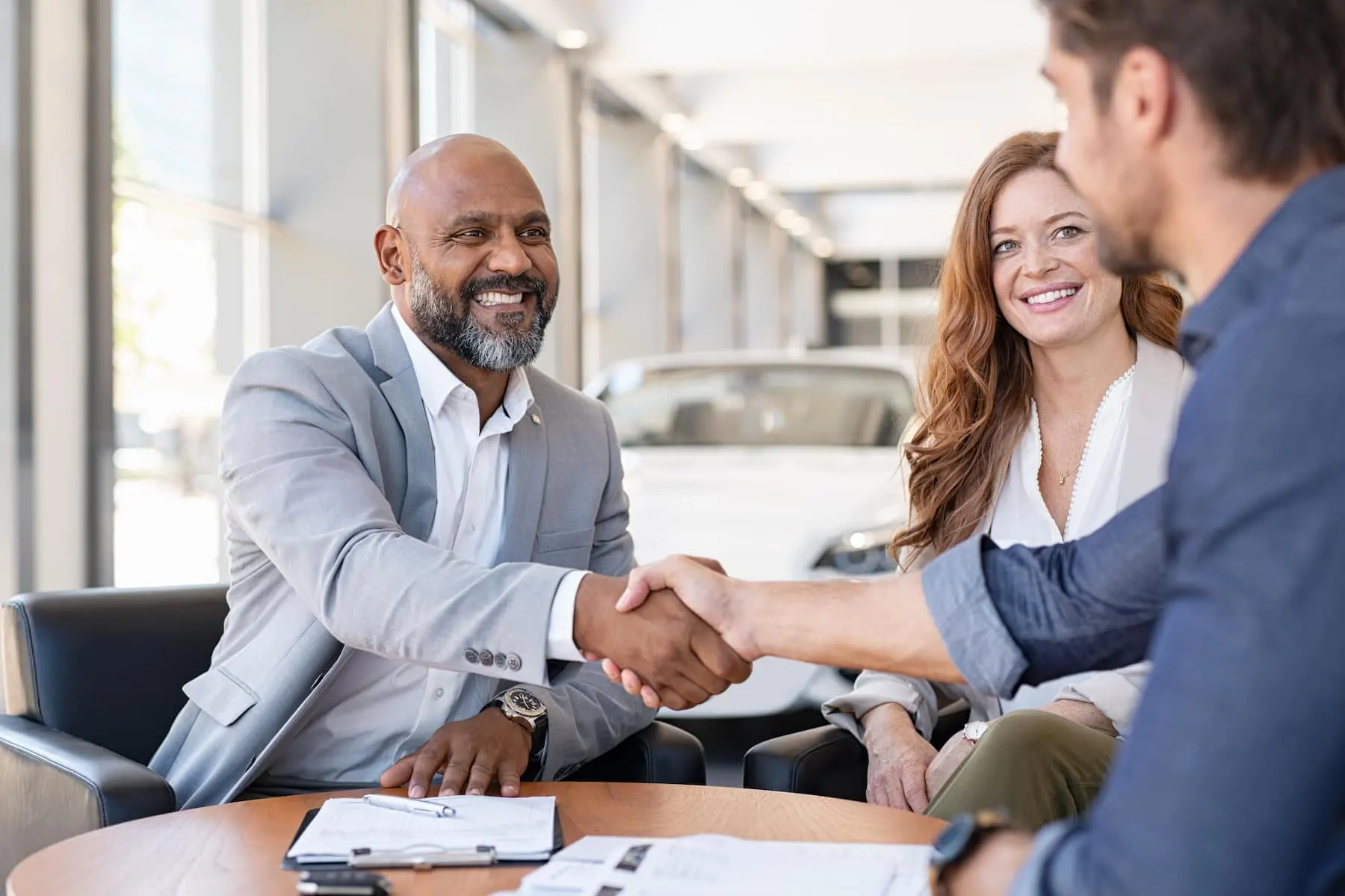 Business people shaking hands over papers at a dealership
