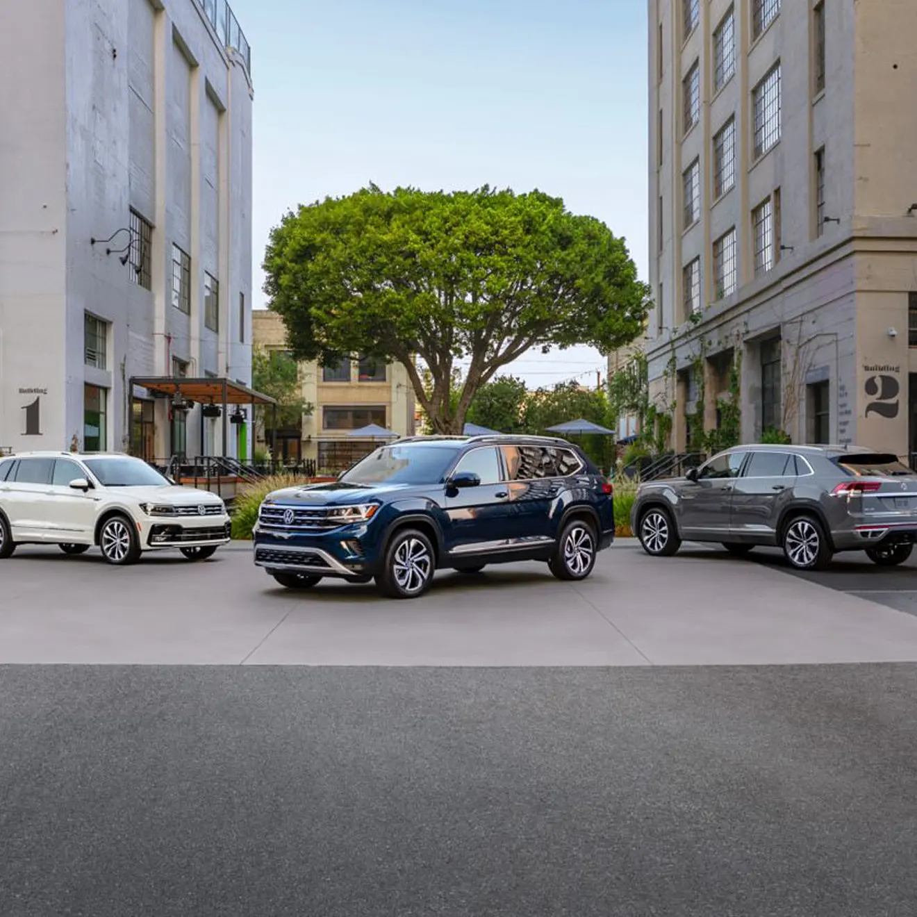 Atlas in Tourmaline Blue Metallic, an Atlas Cross Sport in Pure Gray, and a Tiguan in Pure White are parked on an urban street.