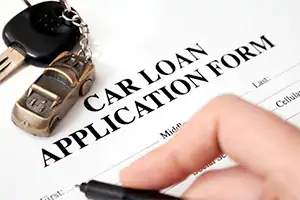 A hand is signing a car loan application form in order to lease or buy a new vehicle.