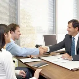 A couple shakes hands with a financial expert on a new financing deal for their car.