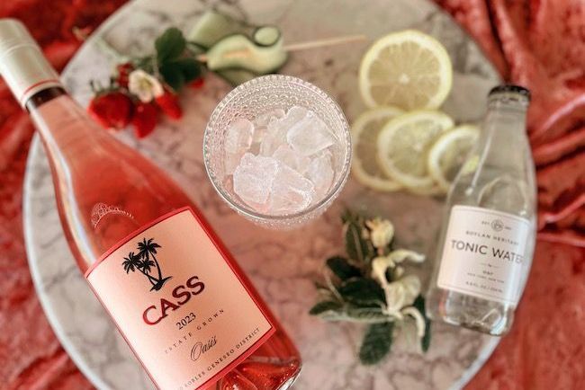 A bottle of CASS Oasis Rosé surrounded by fresh garnishes of cucumber, lemon, mint and strawberries for a classic rosé spritzer recipe 