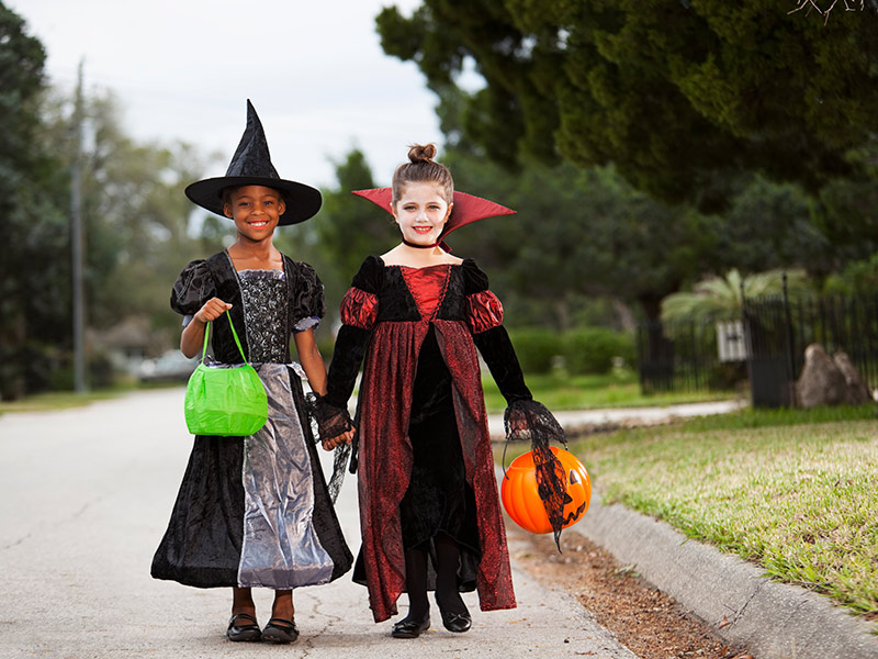 两个小女孩在户外玩不给糖就捣蛋, 一个女孩穿着女巫的服装, 另一个穿着吸血鬼服装