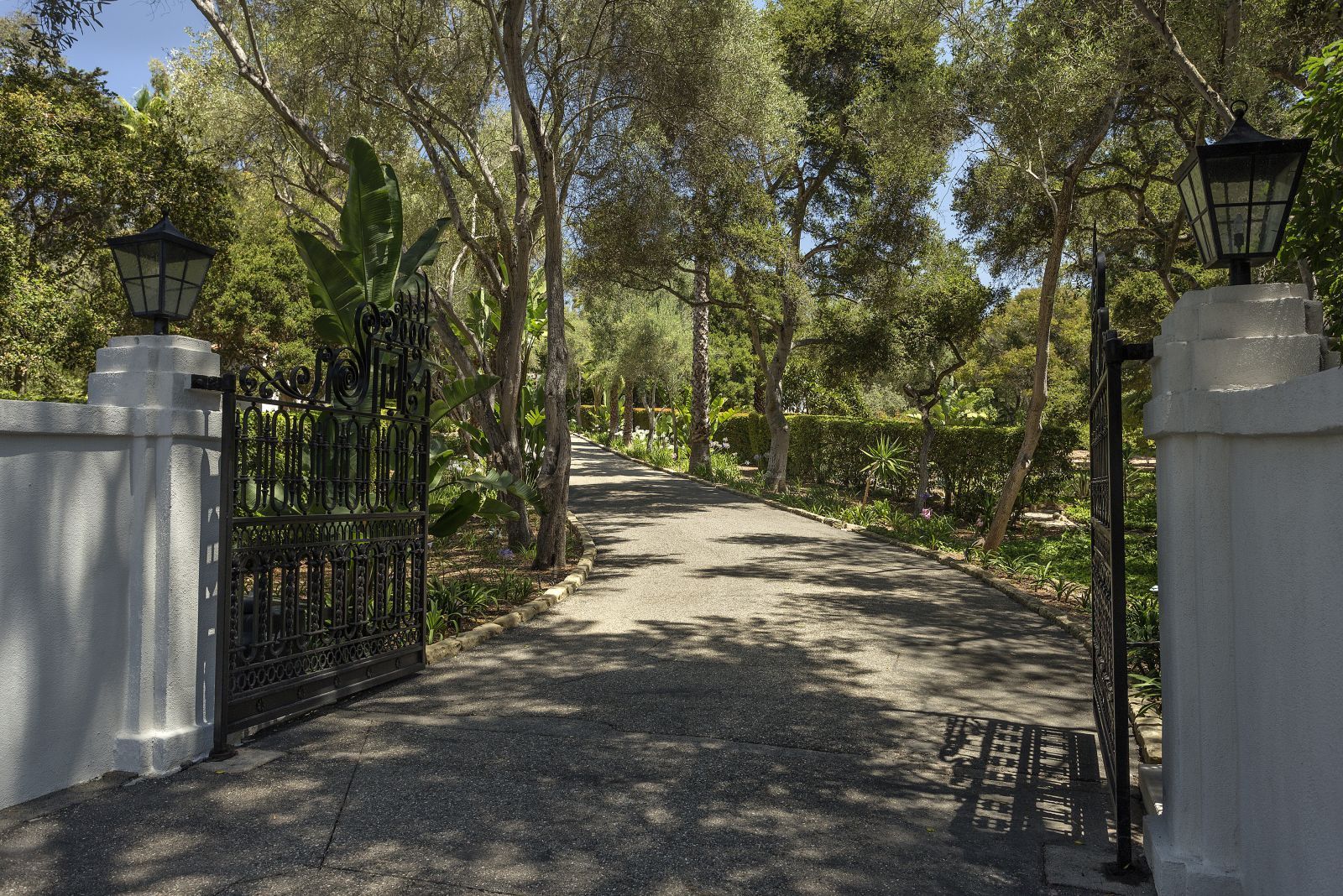 An entry gate opens to a long driveway lined with trees.