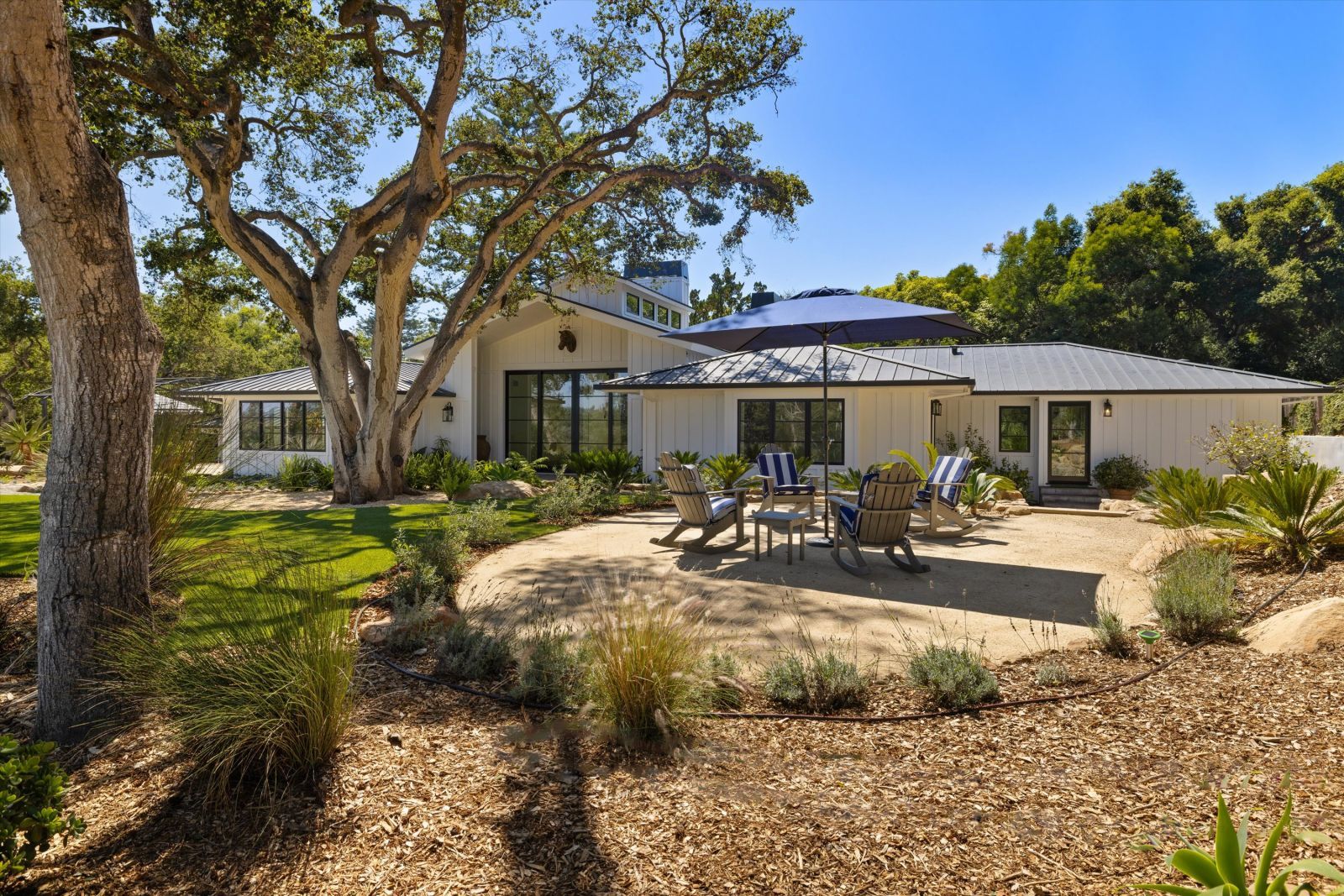 Backyard of a luxury Modern designed farmhouse, with large trees and sophisticated landscaping.