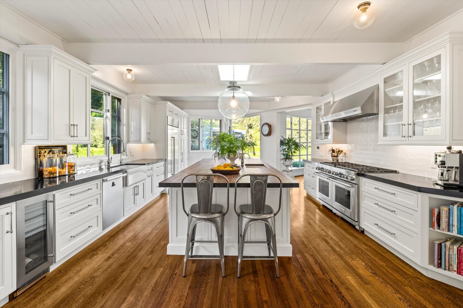 A luxury kitchen with a muti purpose island with stools, a wood floor and an open French door allowing natural light to flood in.