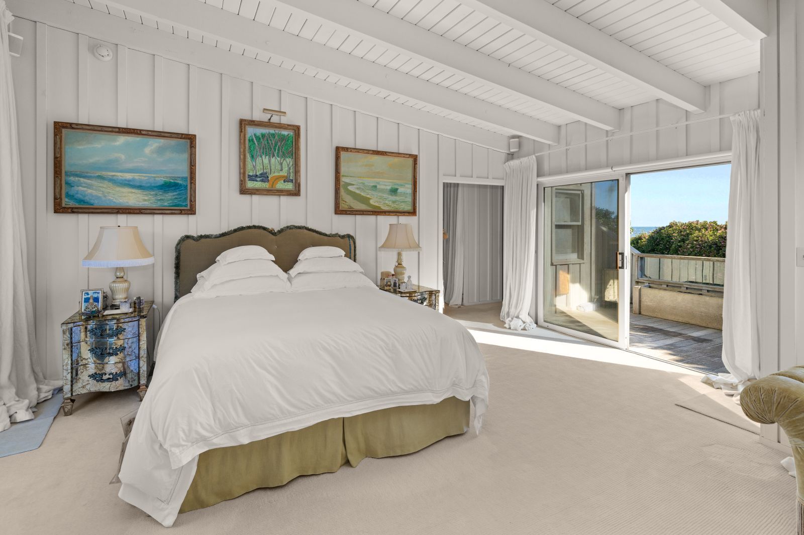 A furnished bedroom in a classic beach cottage with a vaulted ceiling and large sliding glass door open to an outside patio.