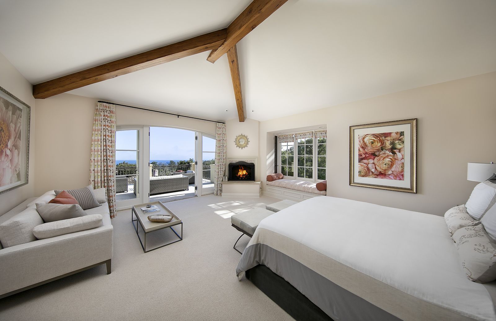 A luxury bedroom with interesting wood beams in the ceiling and a door opening with an ocean view.