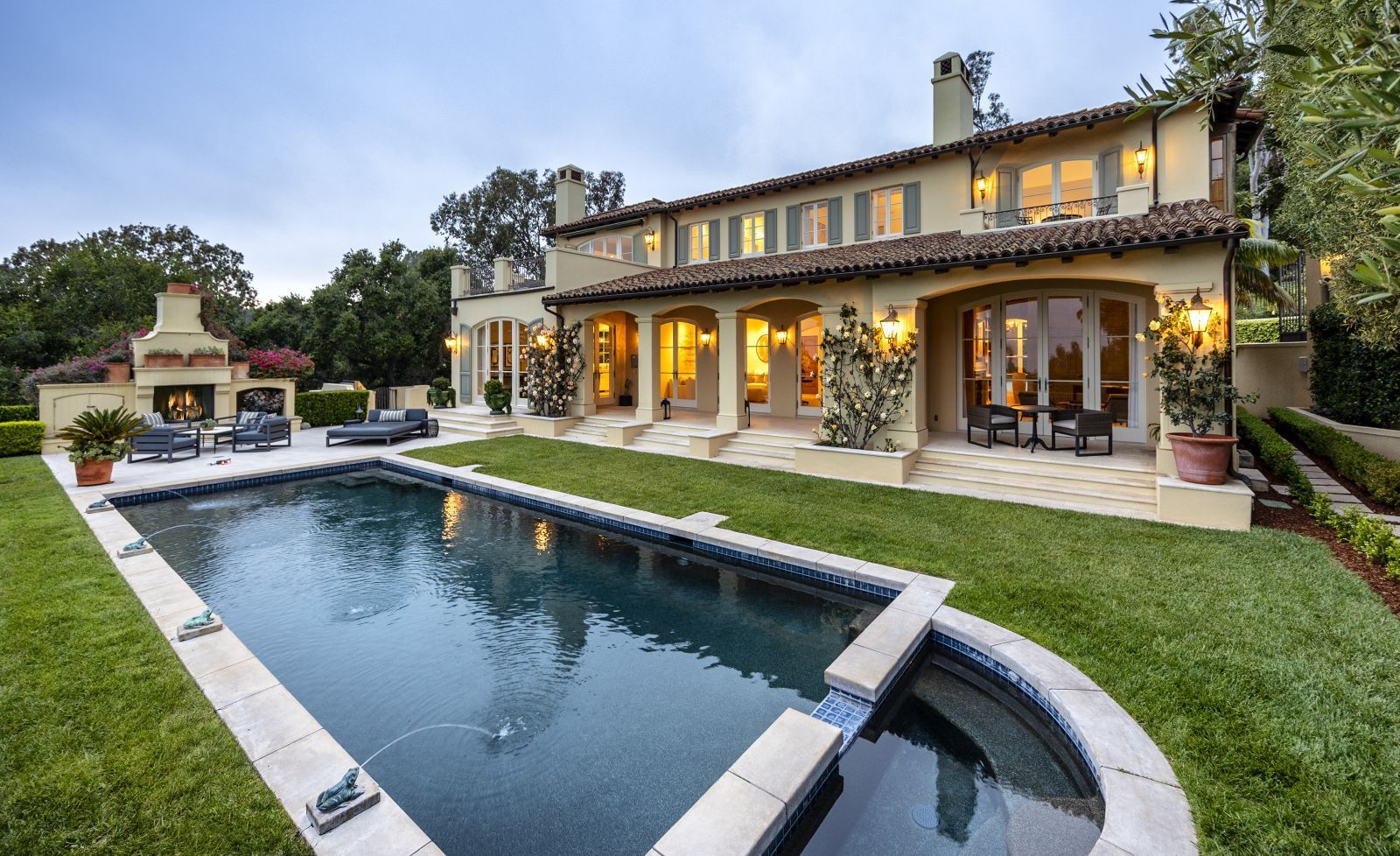 The backyard of a luxury home with a pool, lawn, and fireplace in the foreground
