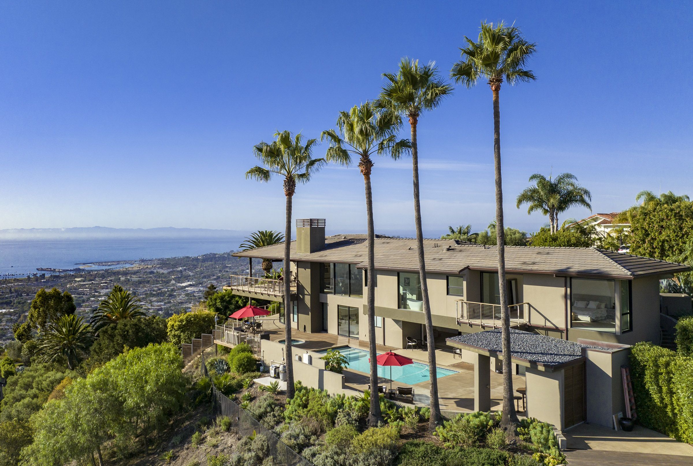 Santa Barbara home on a hill, with 4 tall palm trees in the foreground, overlooking the town and ocean beyond