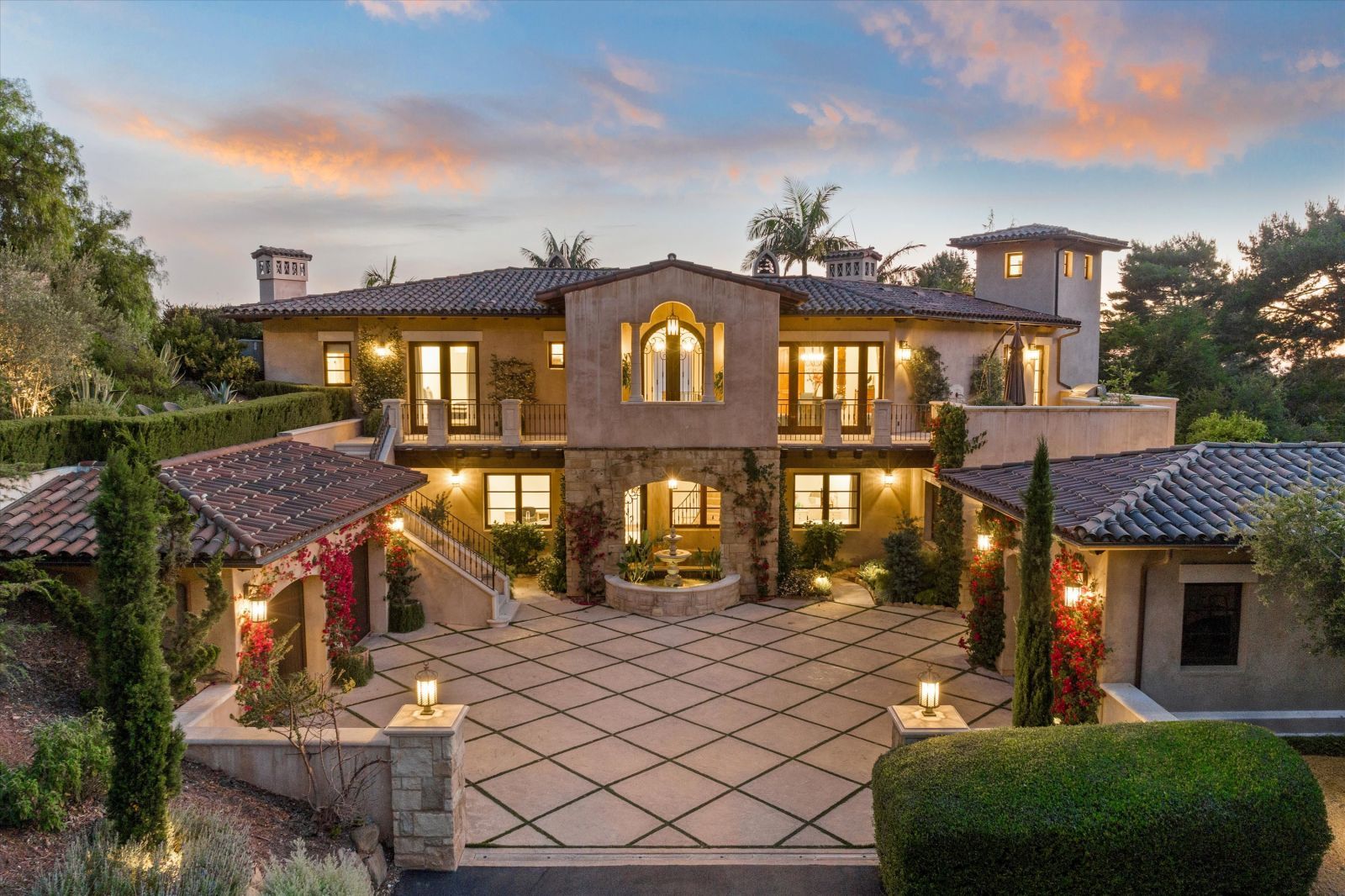 Courtyard of a Tuscan-style luxury home in Montecito, with its lights and the home in the background illuminated.