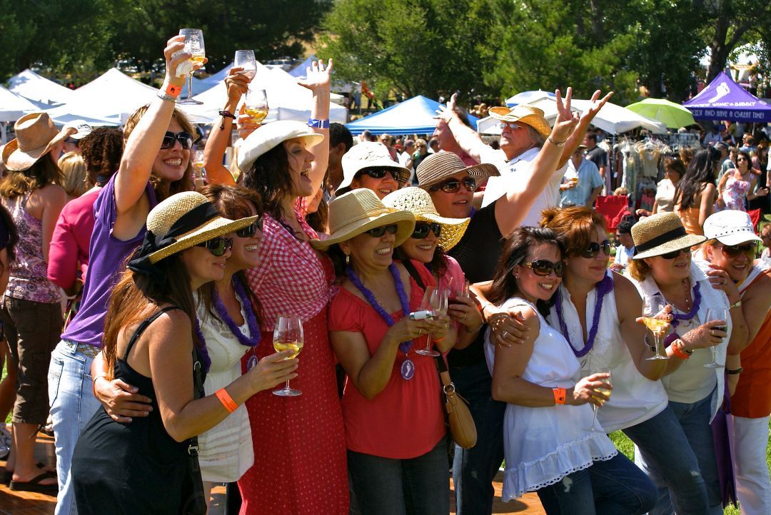 A group of mostly women holding glasses of wine while enjoying live music at a wine festival.