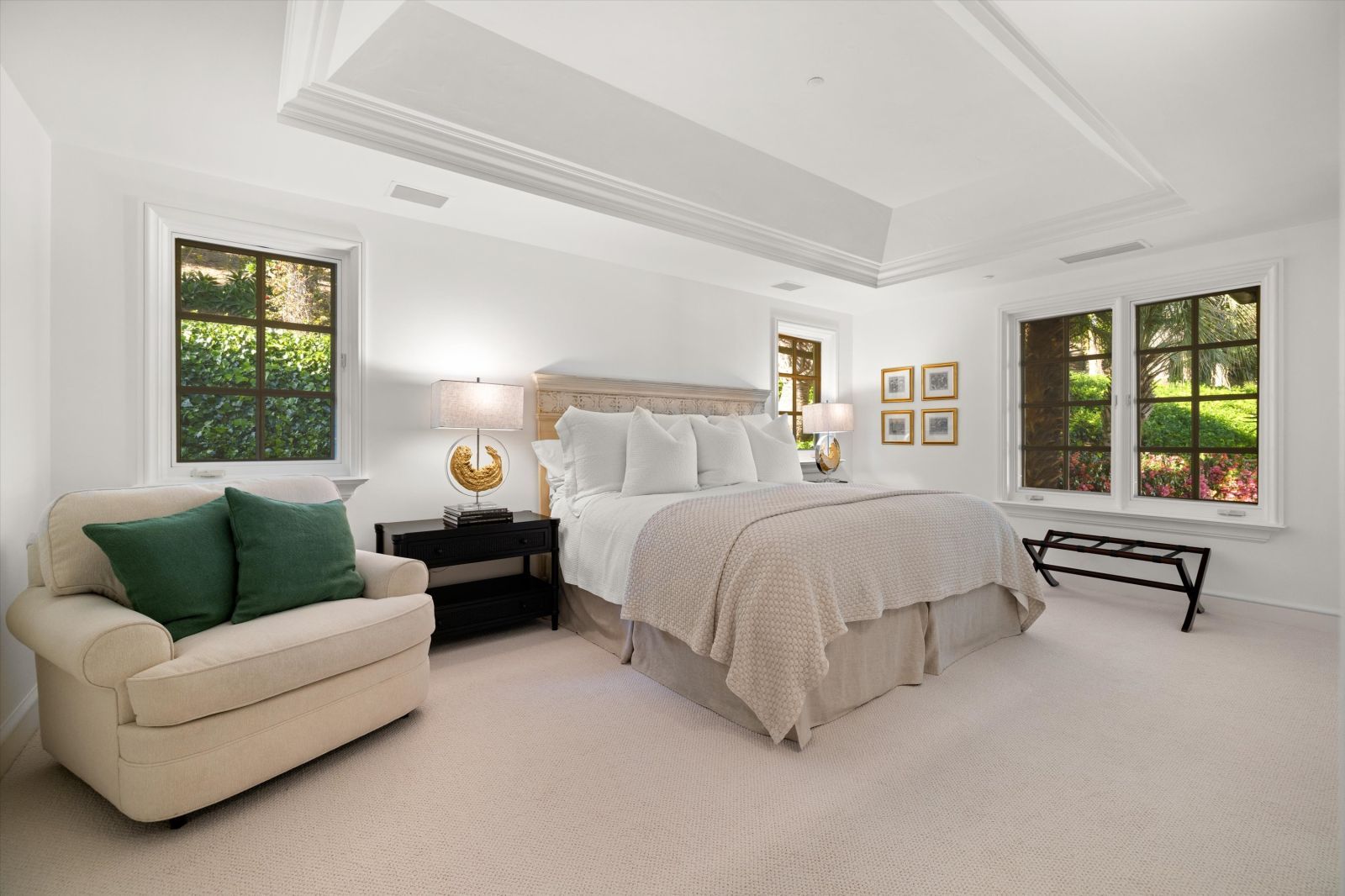 Tranquil designer bedroom with a vaulted ceiling and luxurious shades of beige accented by a pair of rich green throw pillows.