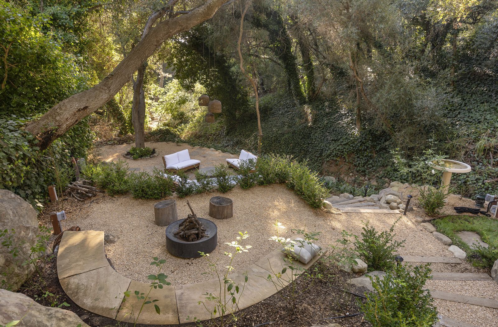 Looking down at a serene oasis in the backyard of a luxury home, with comfy seating, a fire pit, plants and trees at the end of a designer gravel-covered path.