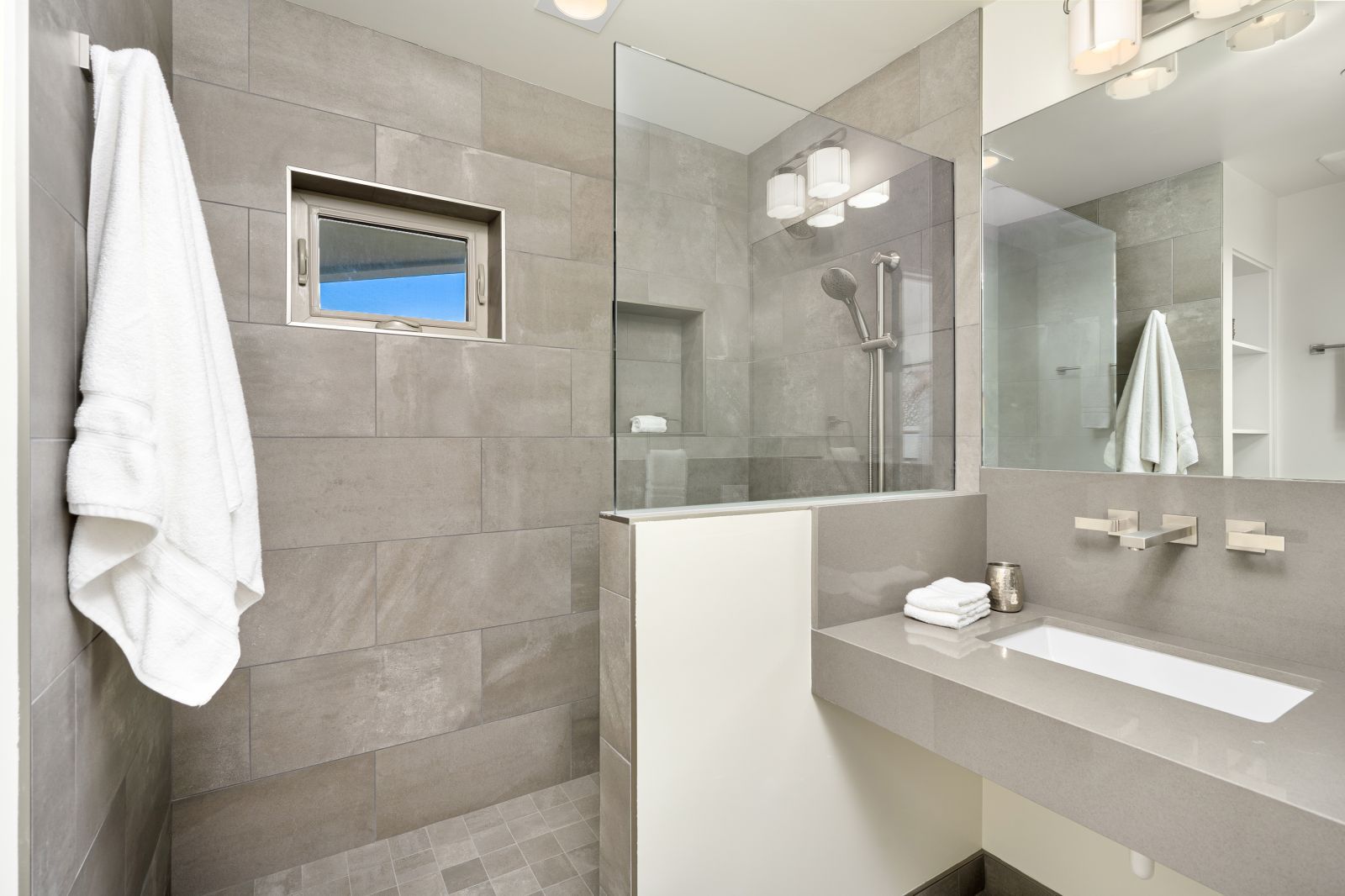 The open shower and adjacent sink of a luxury bathroom with grey stone walls and floor and white towels.