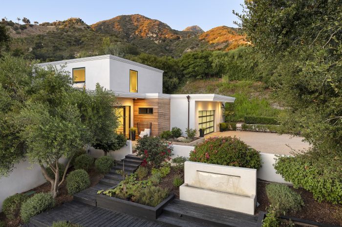 The front of a Montecito Contemporary Ocean View Home, illuminated from within, with mountains in the background at twilight.