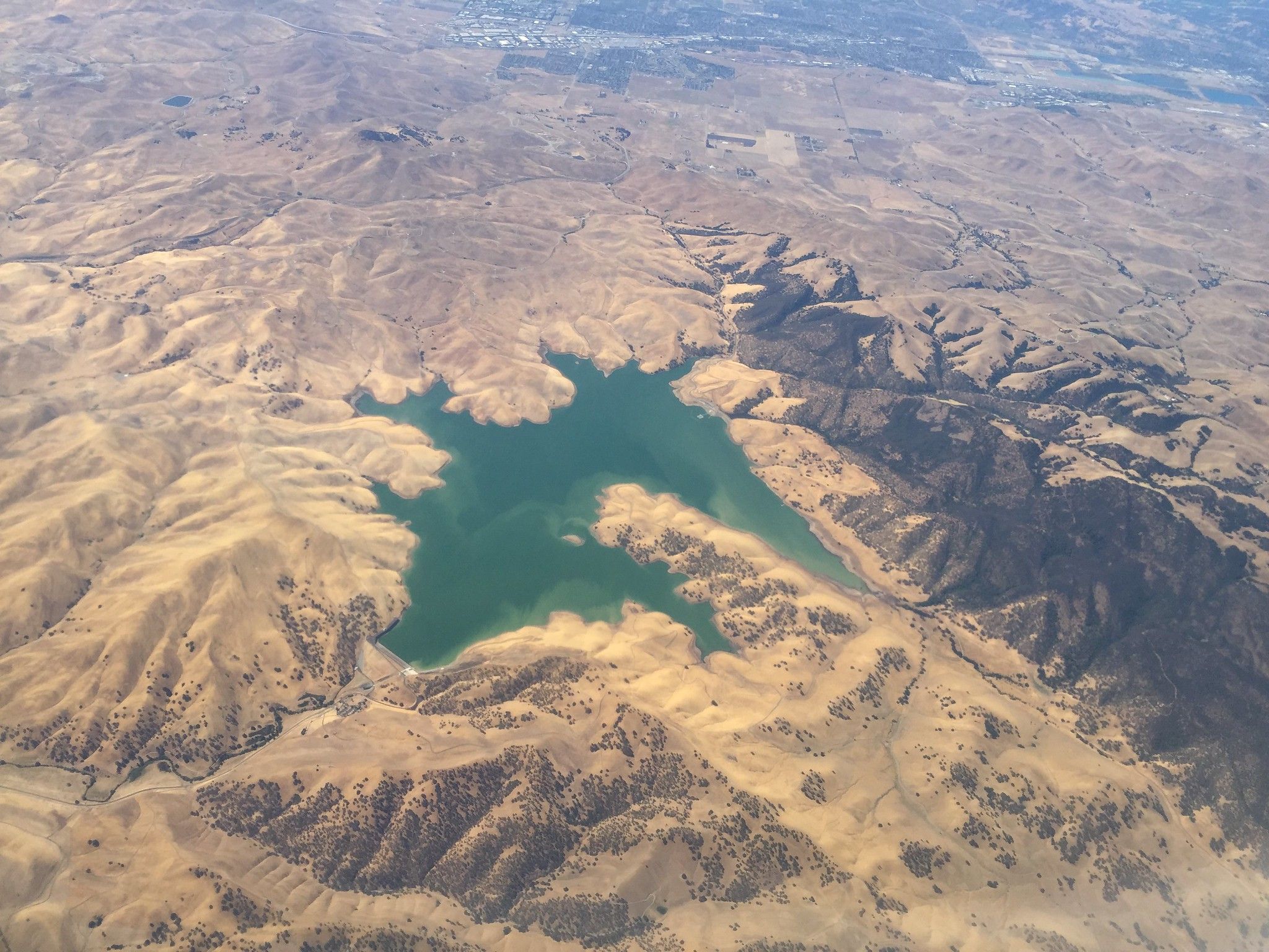 A picture from space of California showing a major drought with little water in a reservoir and lots of dry looking rolling hills.