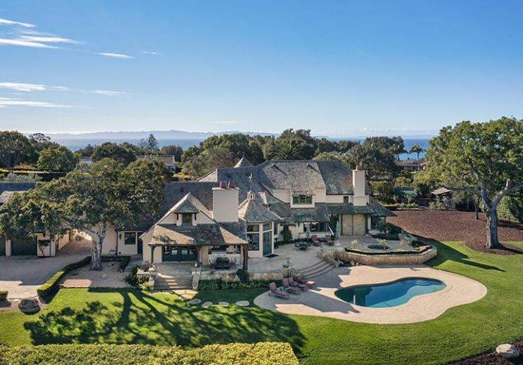 A birds eye view of an English Country style Hope Ranch Estate, with lawn and swimming pool in the foreground and the large home in the background