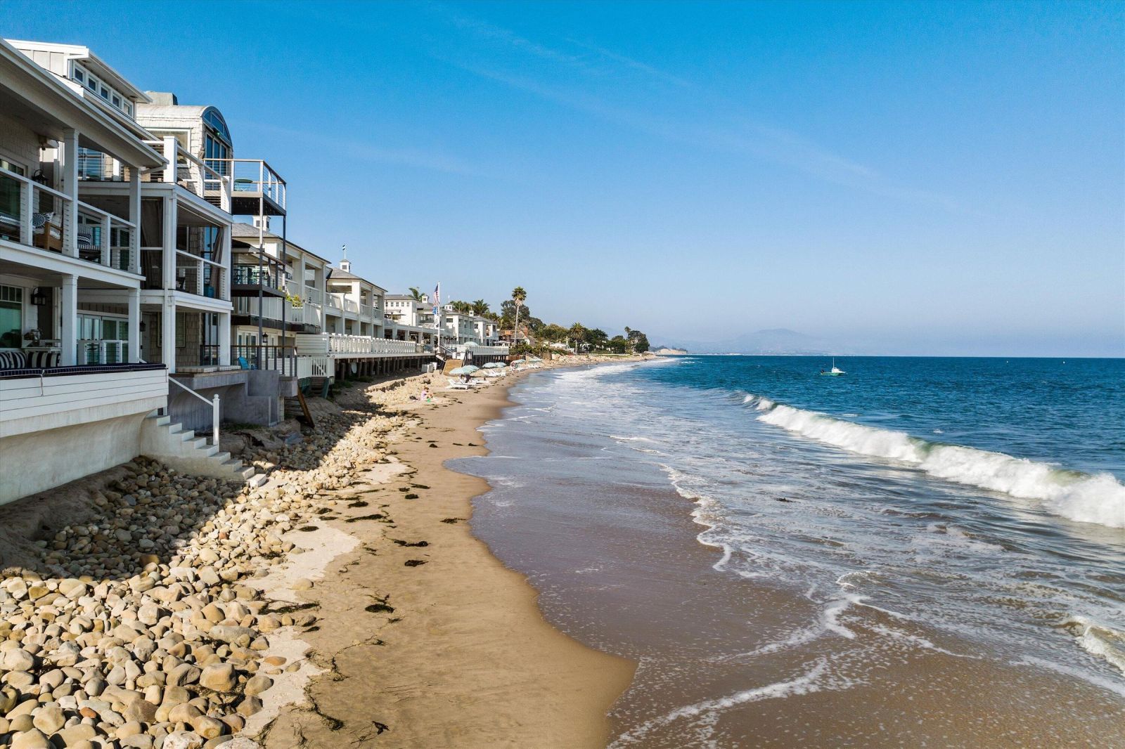 A row of traditional beach homes sitting directly on the sand, with a blue ocean andgentle waves