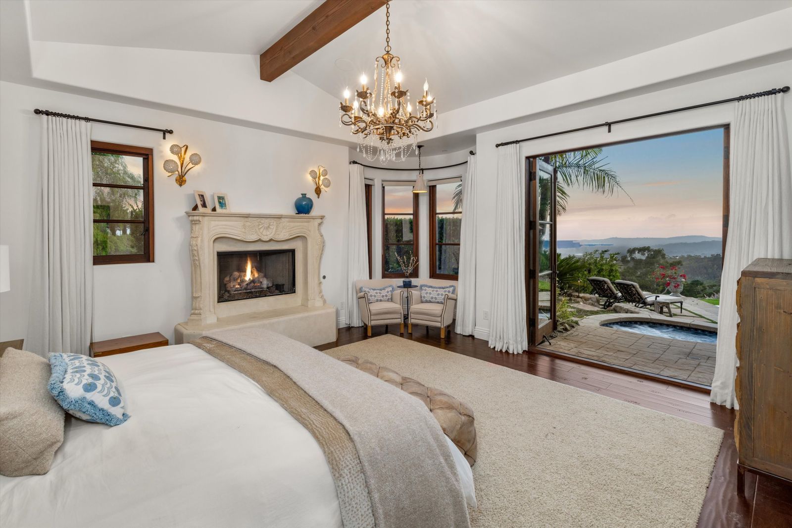 A luxury bedroom with a fireplace and open French doors to an outside pool.
