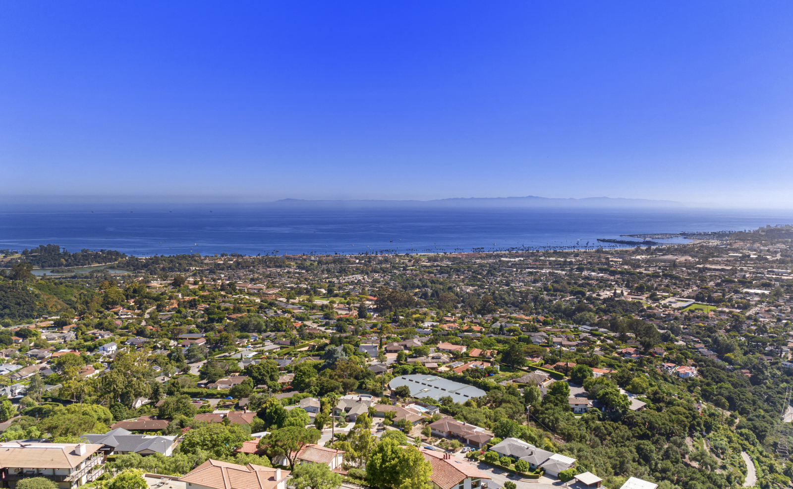 A drone view of the city of Santa Barbara looking out over the neighborhoods to the ocean and bright blue sky