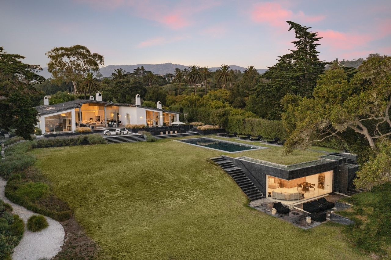 A dramatic bluff top ocean view Hope Ranch Estate surrounded by green trees and grass with a blue and pink sky in the background