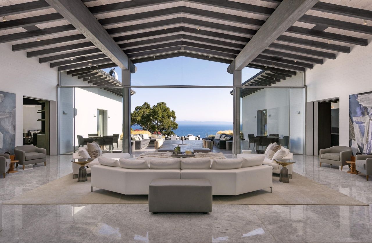 The living room of a luxury estate with floor to ceiling widows that open up to a breathtaking view of the Pacific