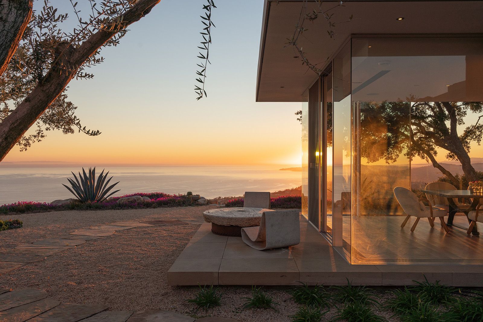A hint of the glass walls and terrace of a contemporary home, looking out to the ocean and setting sun.