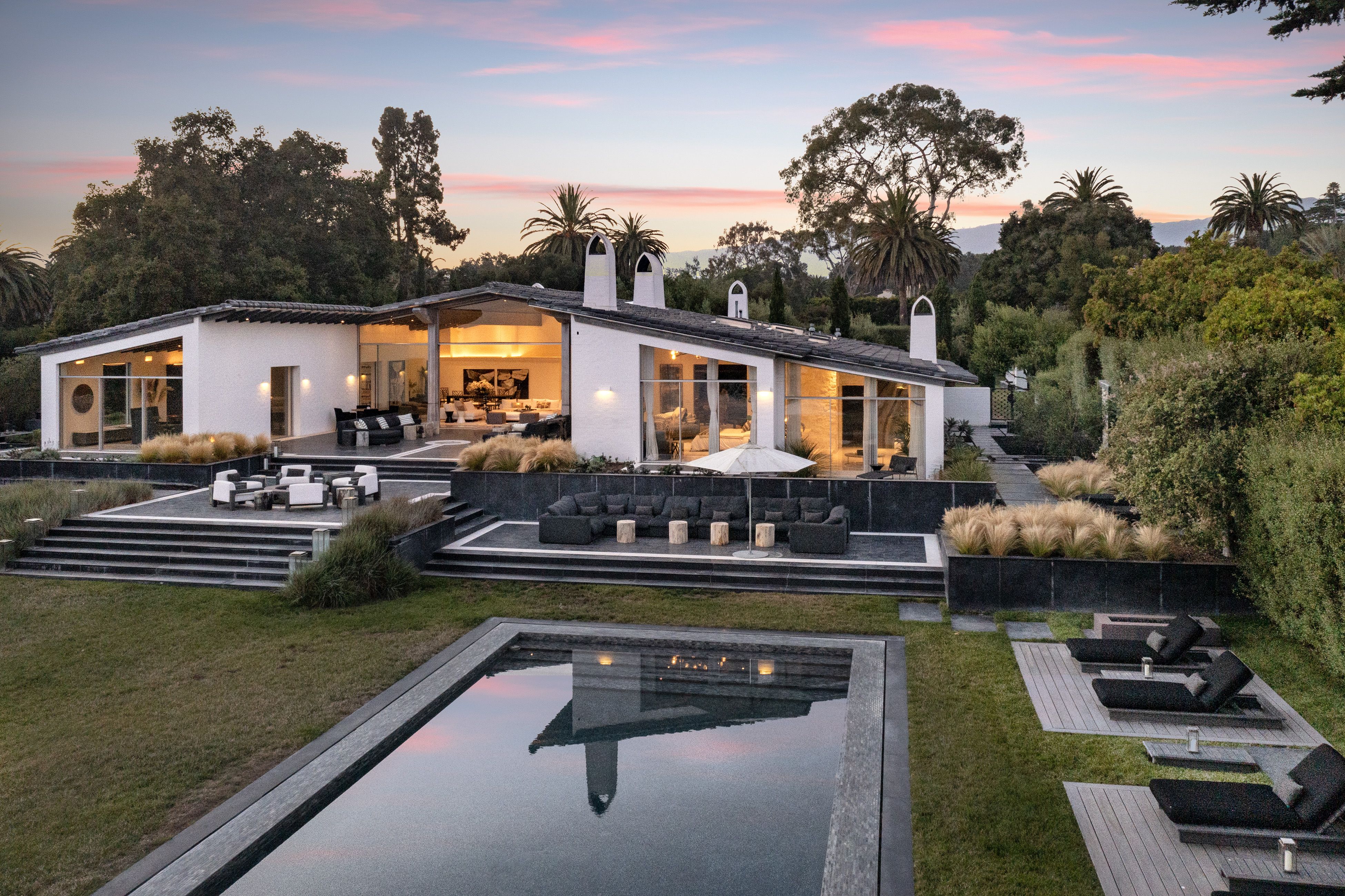 The backyard of a contemporary luxury Santa Barbara home, with a pool and several terraces in the foreground