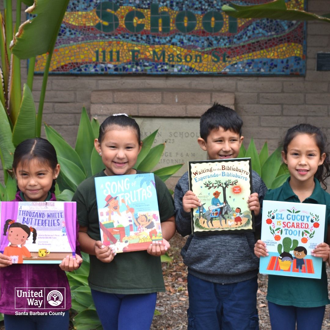 Four smiling youngsters, each holding a children's book in front of plants and a mosaic for the United Way