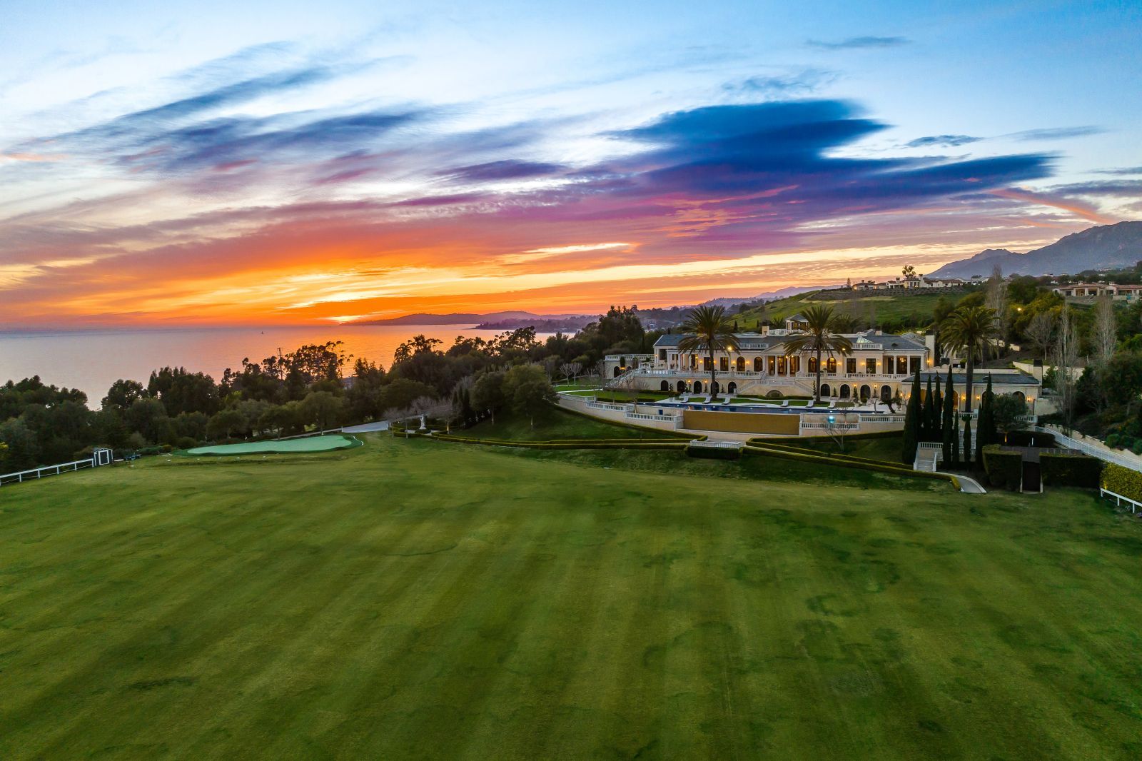 A stunning Santa Barbara sunset above a large estate, with the estate's polo field in the foreground and the massive estate home in the background.