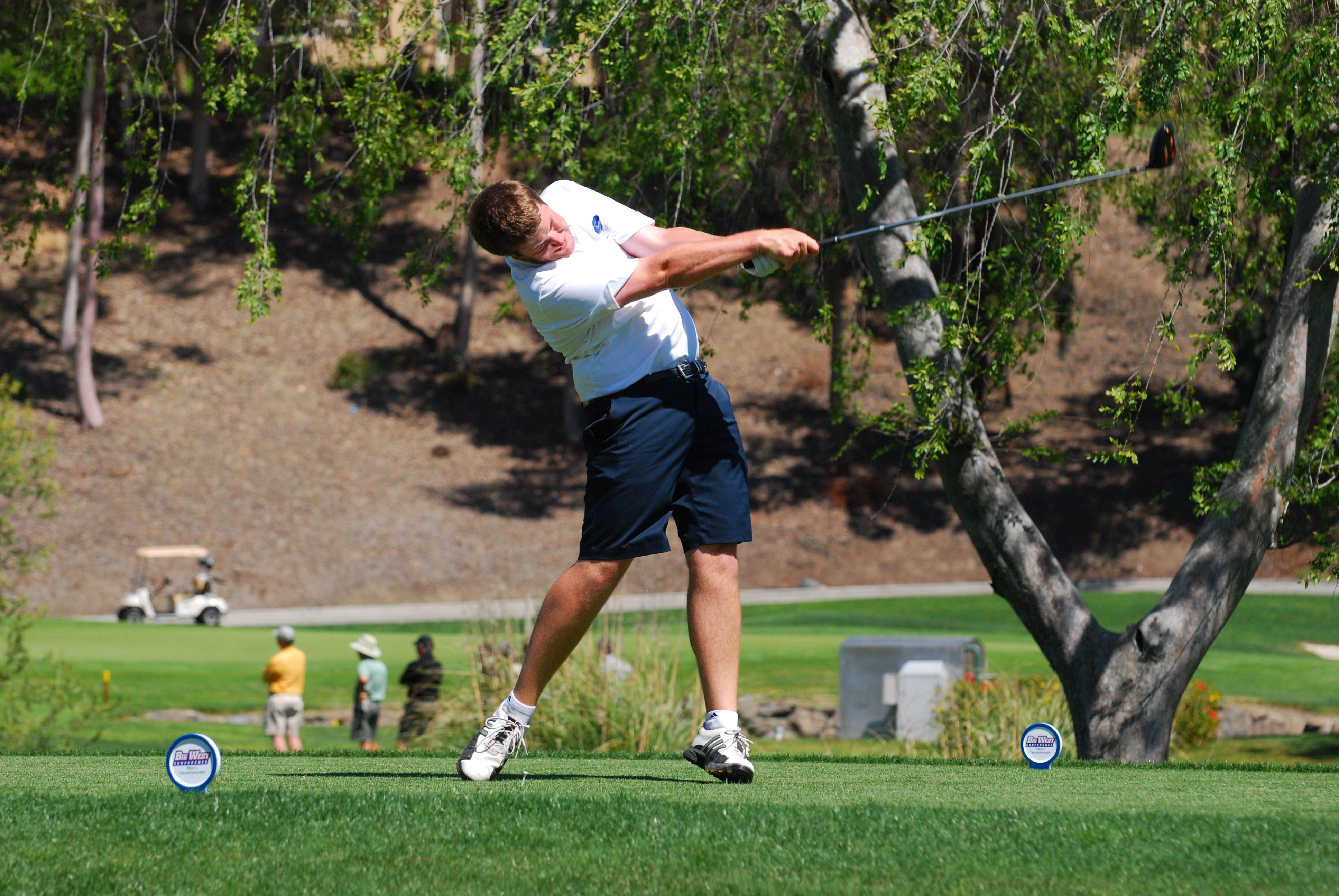 A young man in white shirt and dark blue shorts hitting a drive on one of the Santa Barbara golf courses