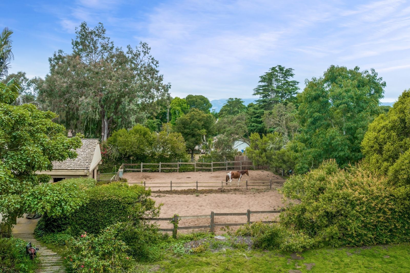 The barn and paddock of an equine estate in Hope Ranch, with a horse standing in the paddock.