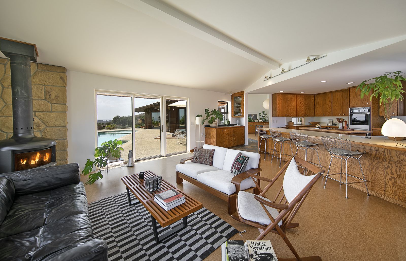 A comfortable keeping room with a fireplace next to an upscale home kitchen with a view through a sliding door to the pool outside