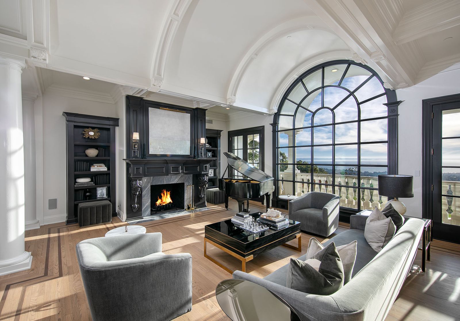 Living room of a luxury home, with a fireplace, floor to ceiling curved and multi-pane window, and luxury furniture