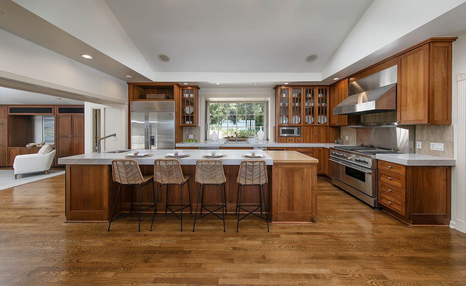 A stylish high-end kitchen with a tray ceiling, wood floors, top of the line appliances, and 4 chair back stools in front of a serving island