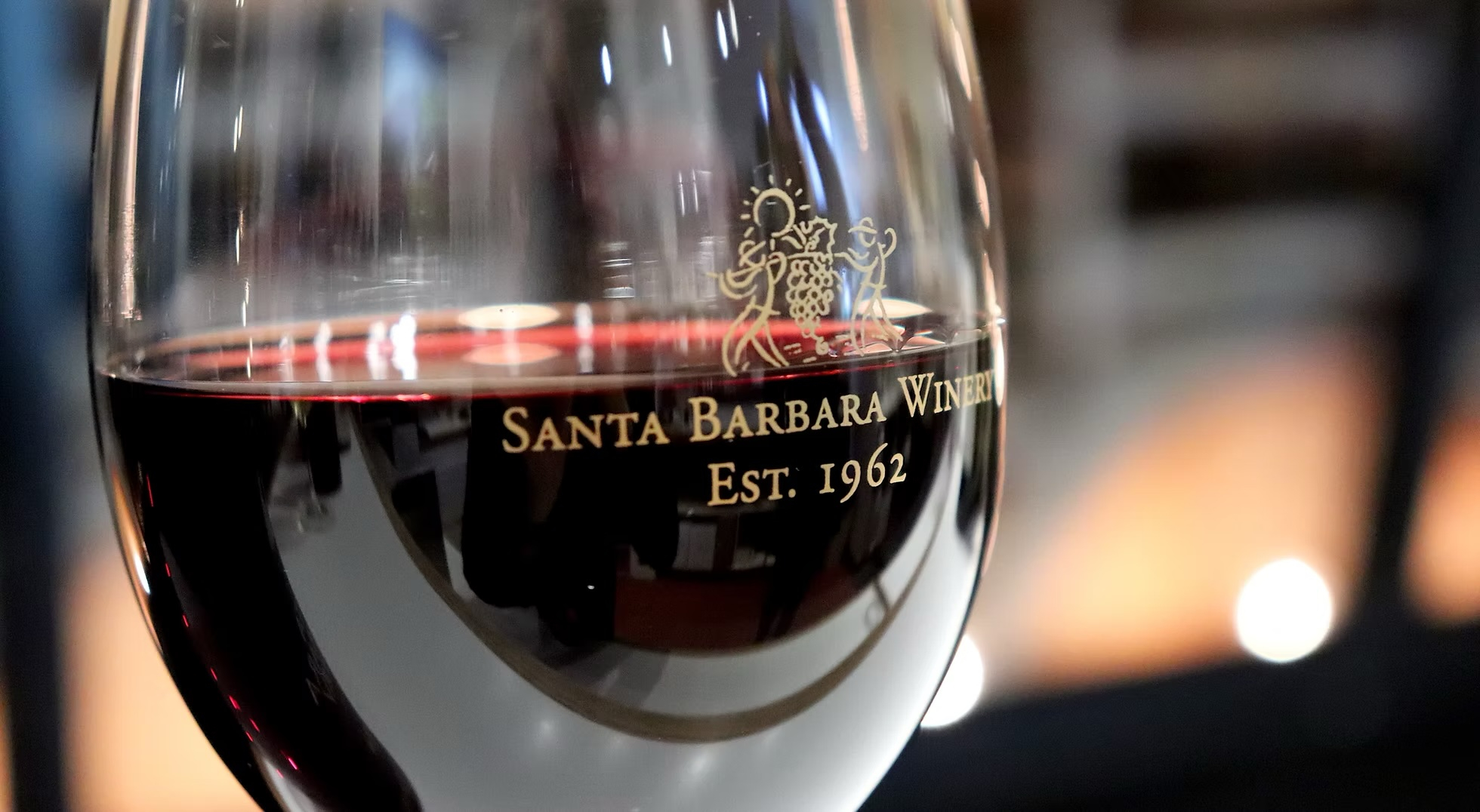 Close up of a wine glass filled with red wine with the Santa Barbara Winery logo.
