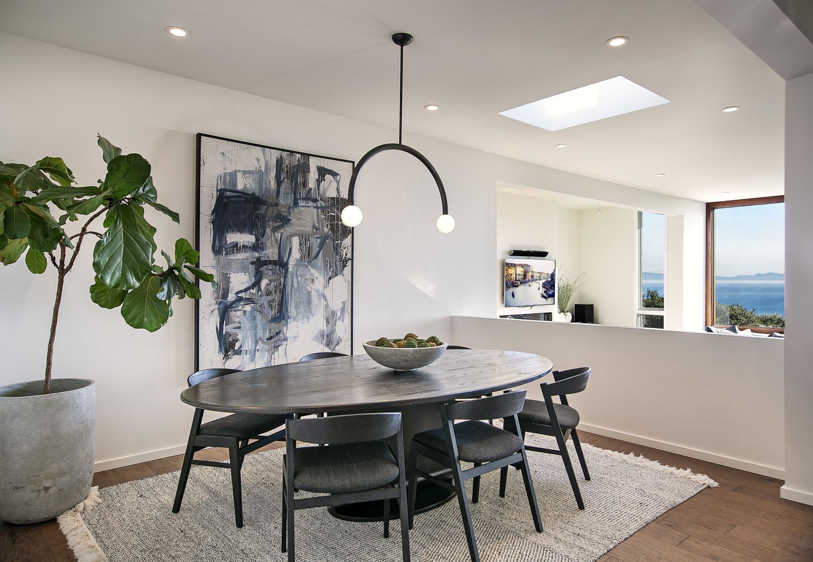 A formal dining room with a modern light fixture above a black table with a breathtaking ocean view.