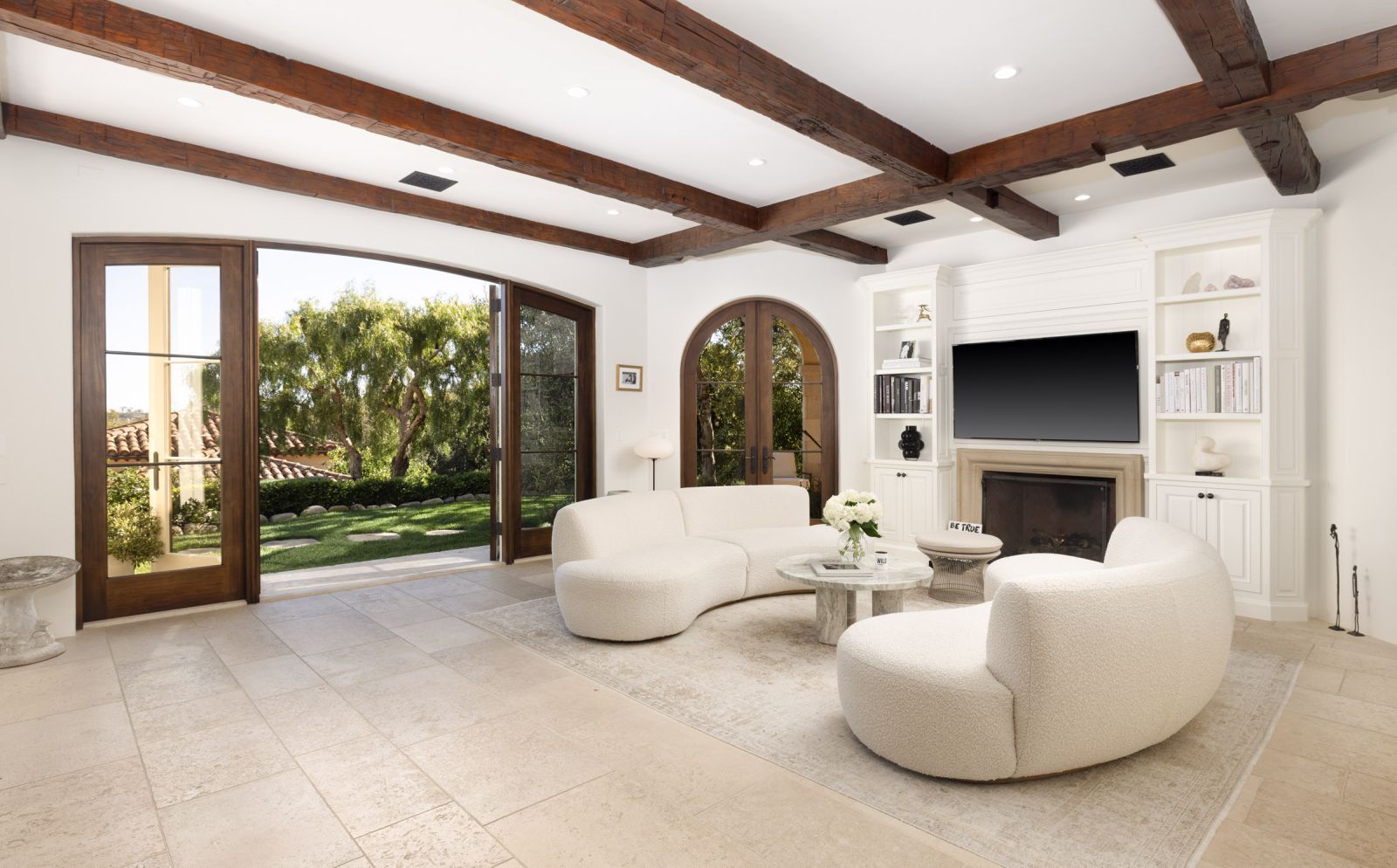 A sunlit room with hardwood floors, exposed wood beam ceiling and French doors leading to the backyard.