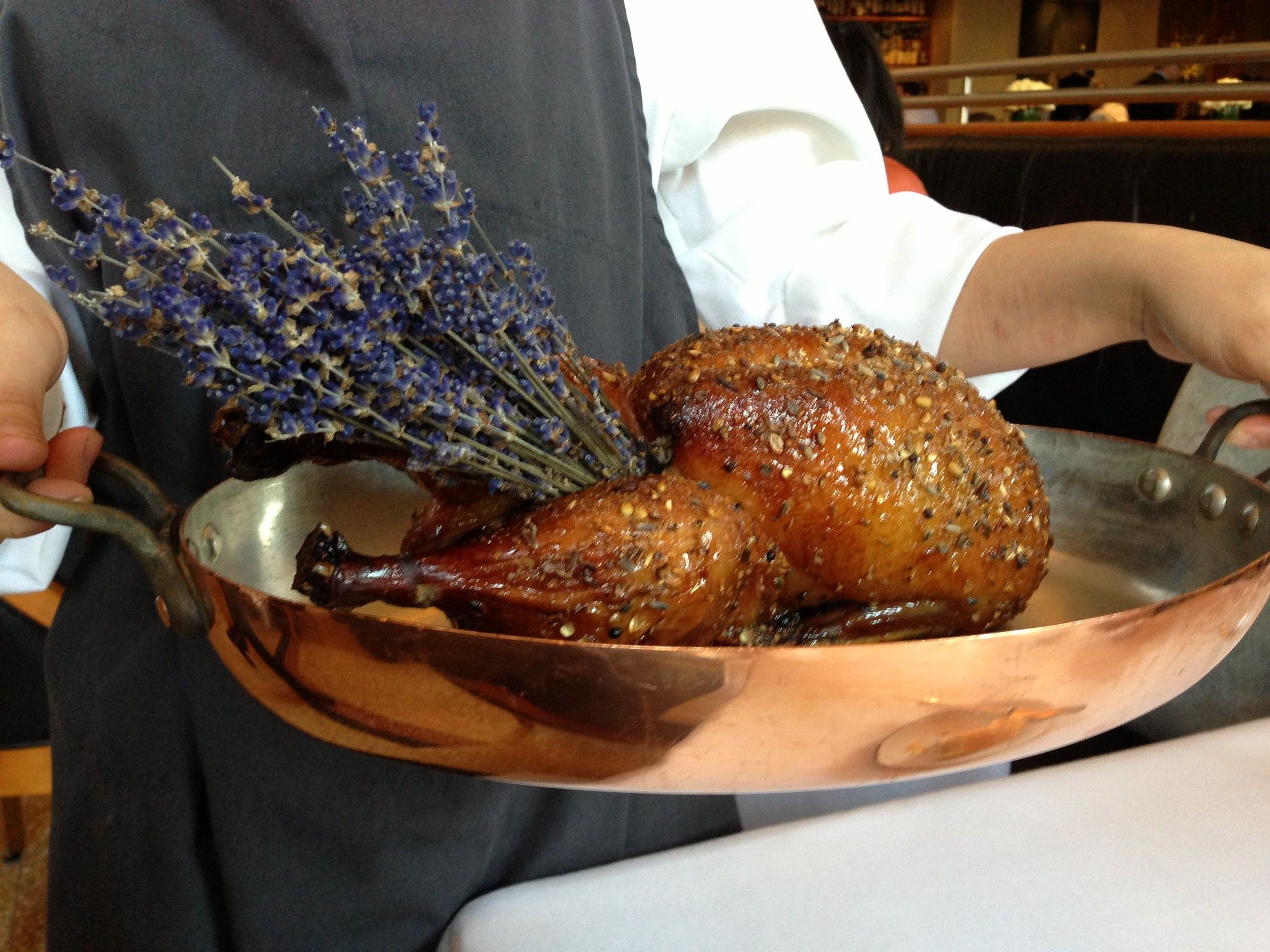 A chef holding a copper pan containing a roasted fowl with sprigs of fresh lavender extending from its cavity.