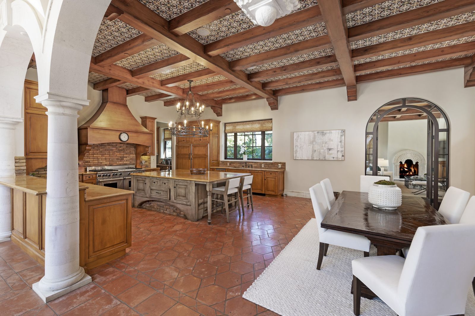 an open florplan kitchen and dining area, with terra cotta floor, an open wood beam ceiling, and a brick backsplash in the kitchen.