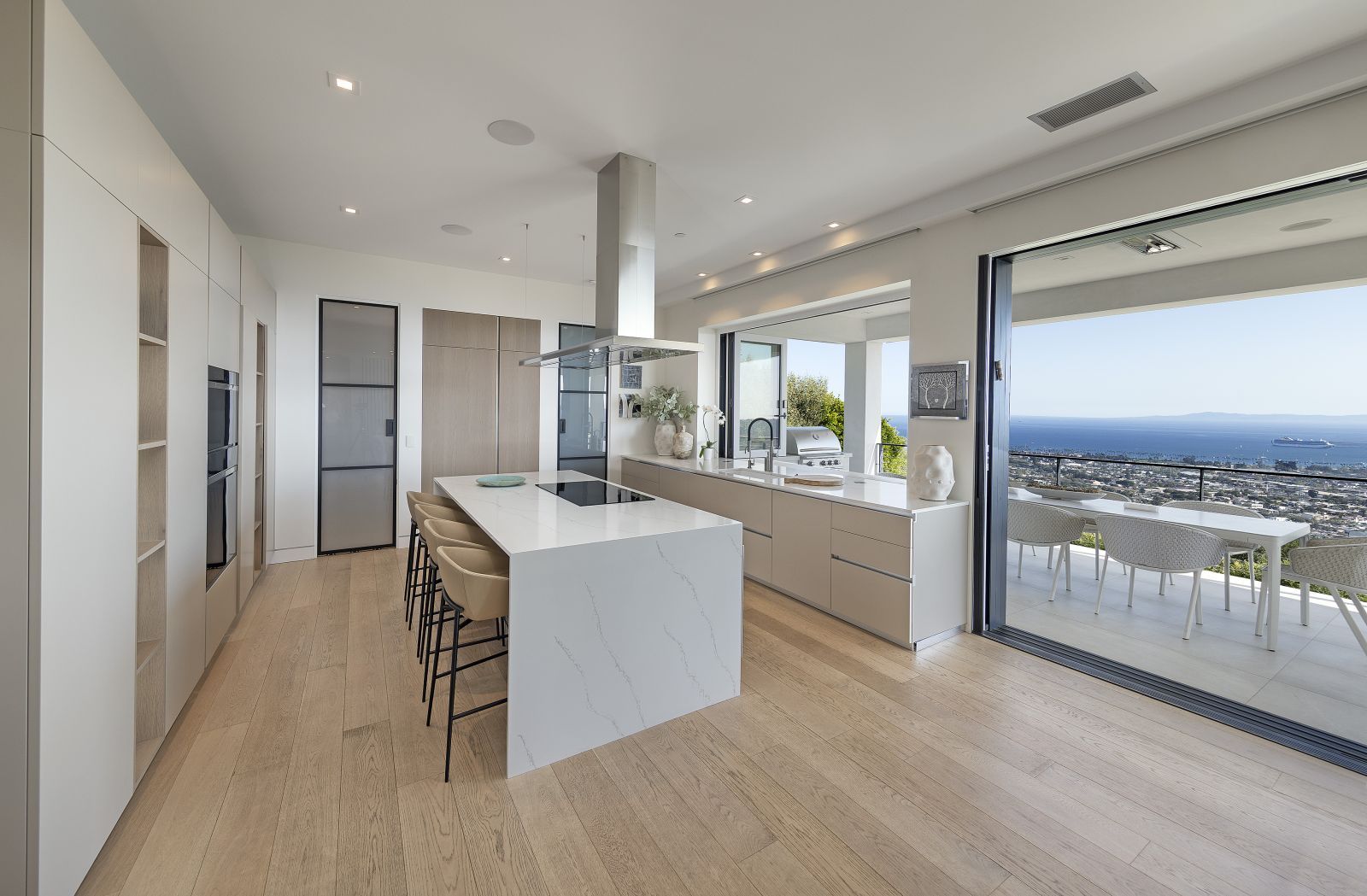 A sleek, gallery style white kitchen with top of the line appliances and breathtaking ocean view.
