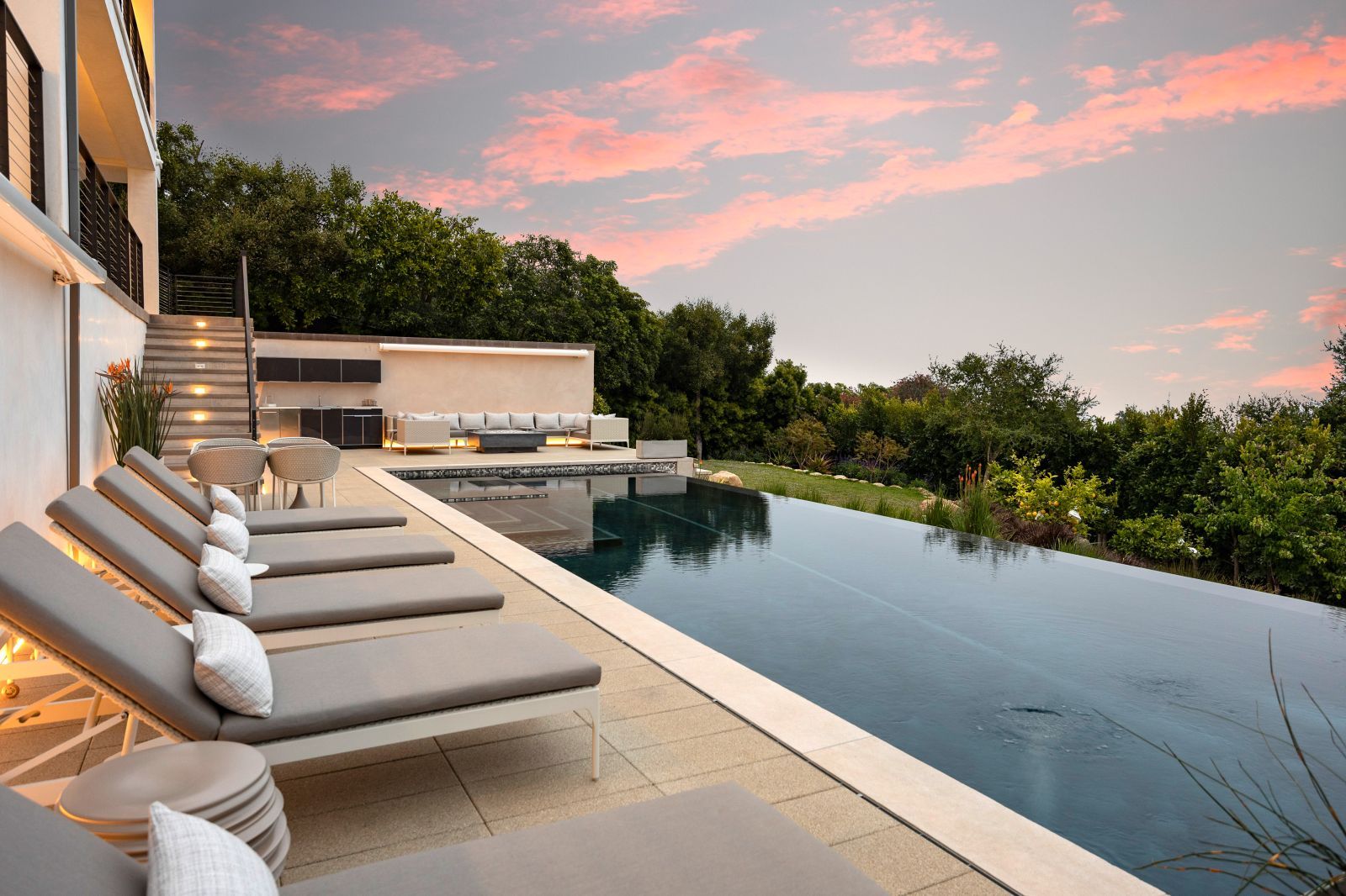 An infinity pool and several lounge chairs with a breathtaking pink and blue sunset.