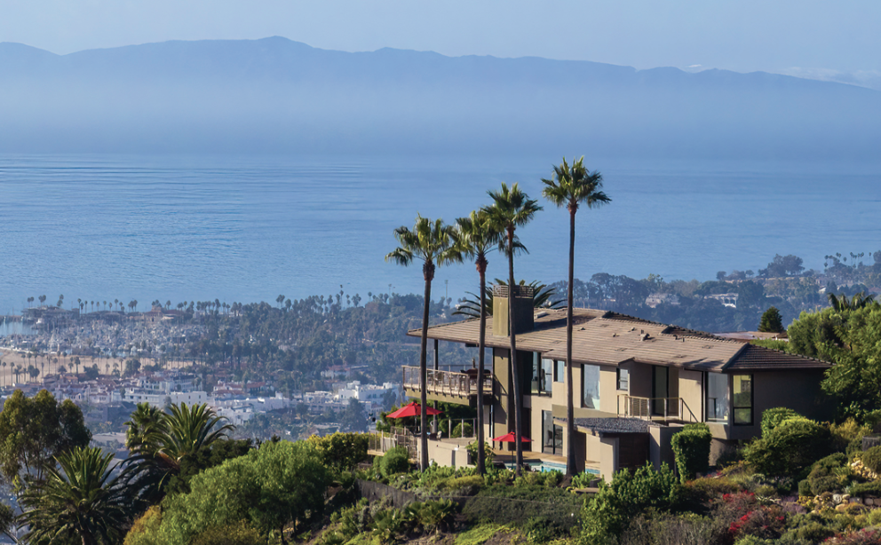 A contemporary home perched above Santa Barbara, with palm trees and a view of the city, ocean, and Channel Islands in the background