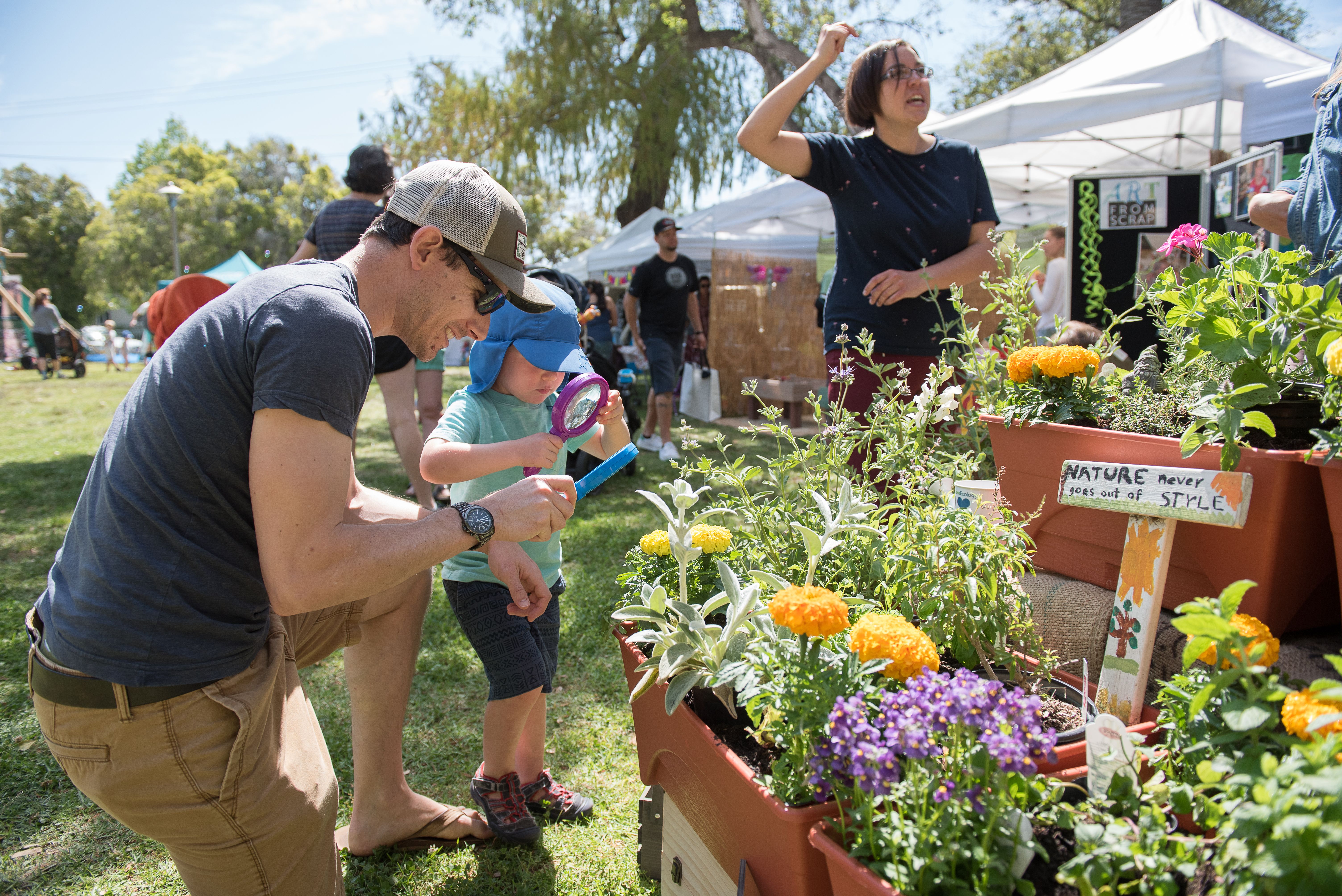 A young father and a toddler looking at green plants and flowers at Santa Barbara Earth Day festivities.