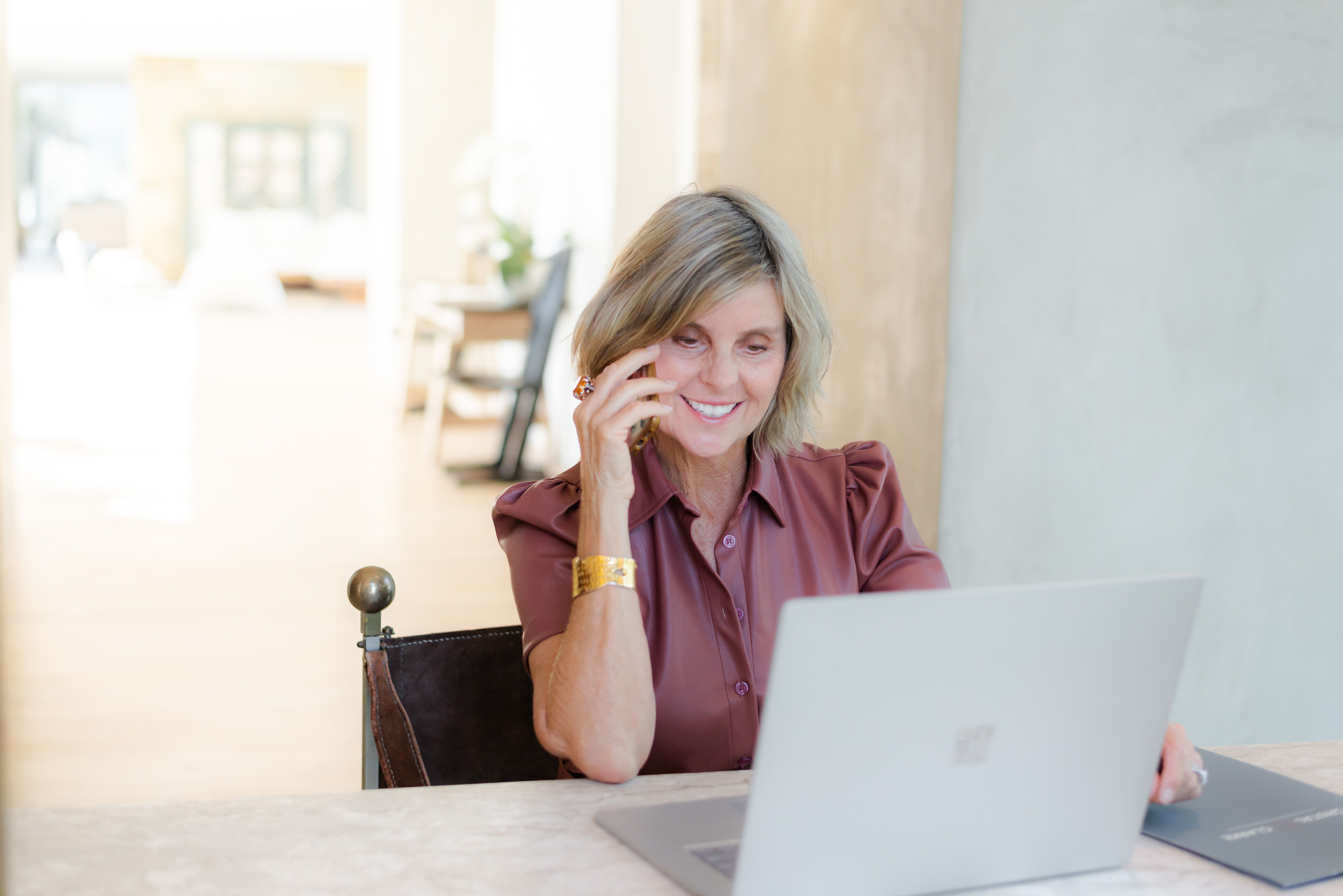 Business woman smiling behind a desk and looking at laptop computer while on the telephone.