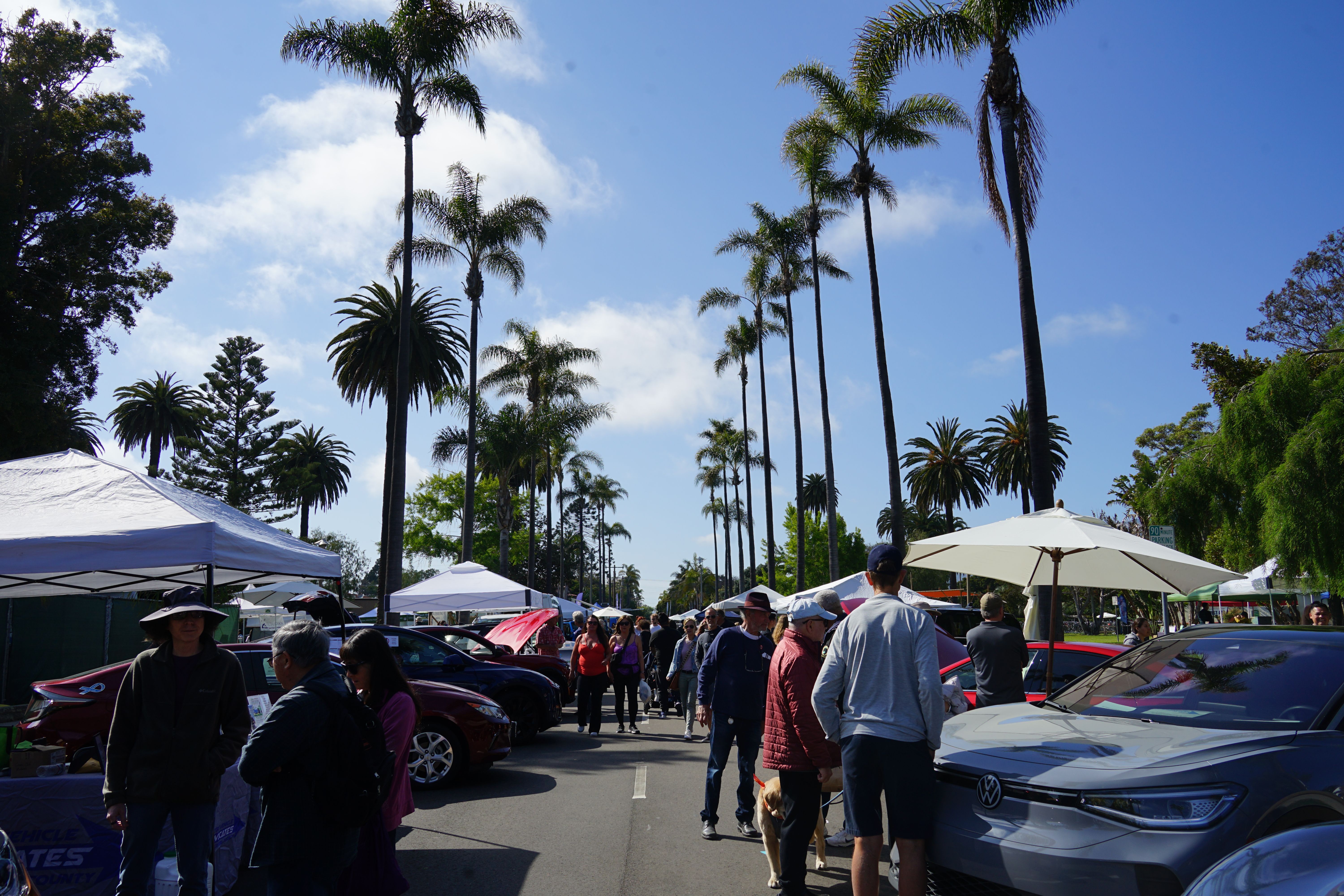 Booths lined up at Santa Barbara Earth Day with electric cars and people in the foreground.