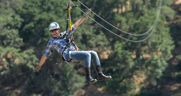 Happy helmeted man dangling from a zipline, with trees in the background