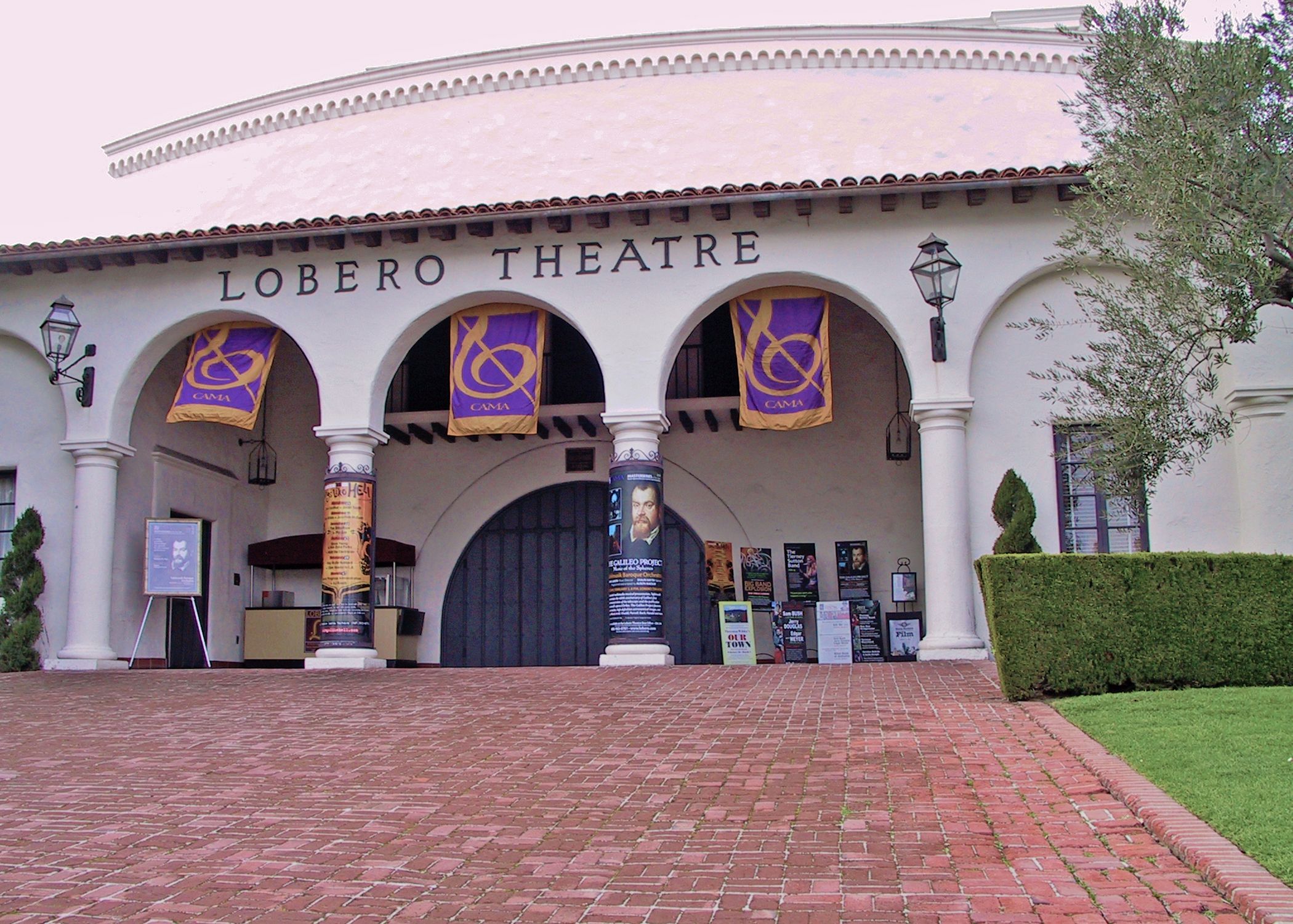 The front of the Lobero Theater with its red brick sidewalk and columns with banners hanging from the arches