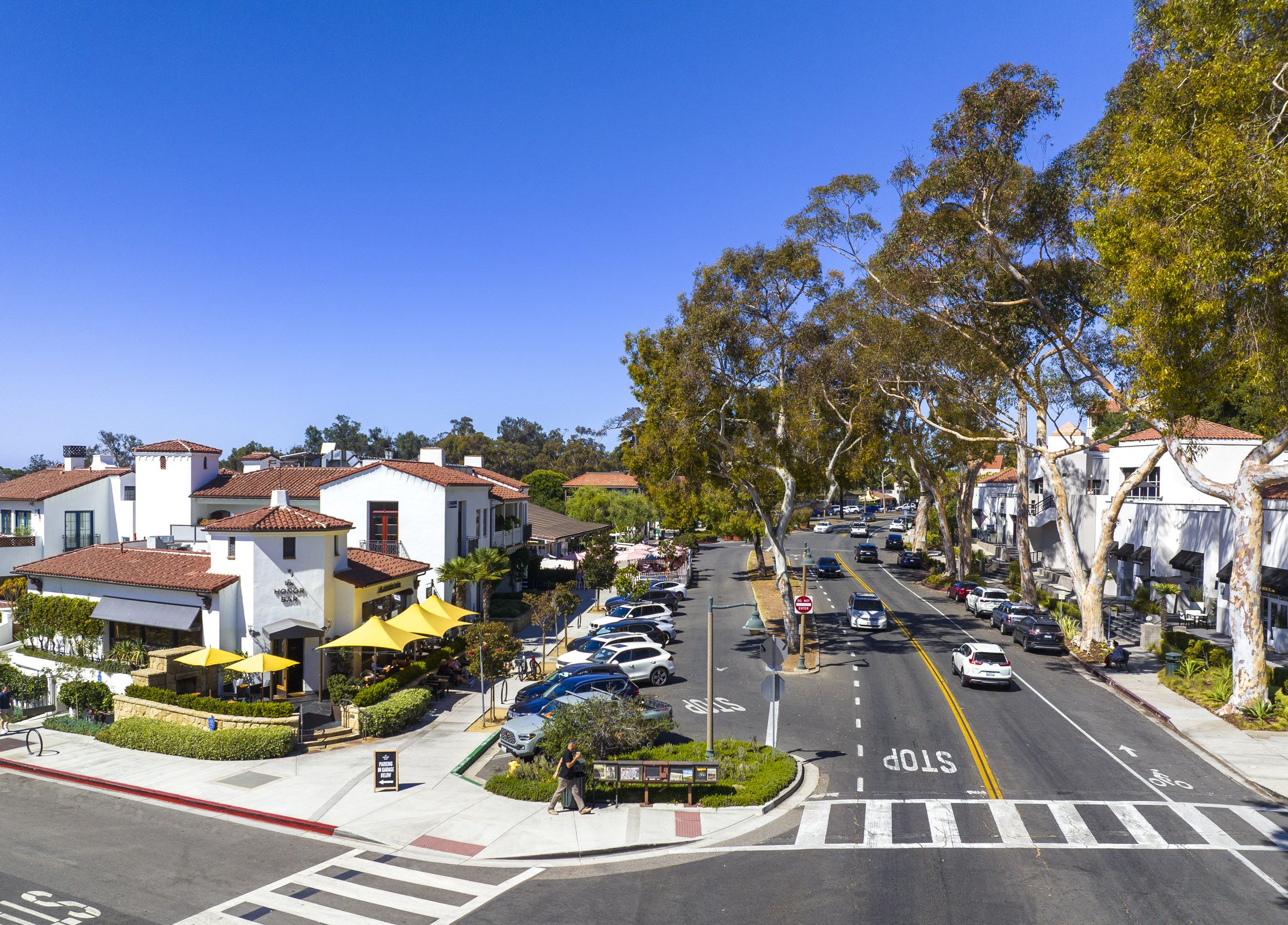 A birds eye view of Coast Village Road, the picturesque street in Montecito, showing white buildings with red tile roofs and a landscaped boulevard